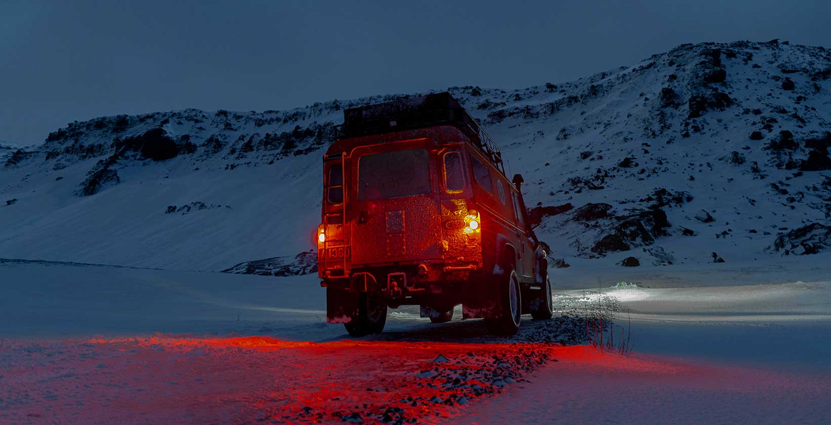 Defender avec feux arrière rouges dans un paysage enneigé au crépuscule